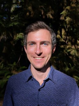 headshot of Joel Gibbs with a blue shirt and a vignette background of trees